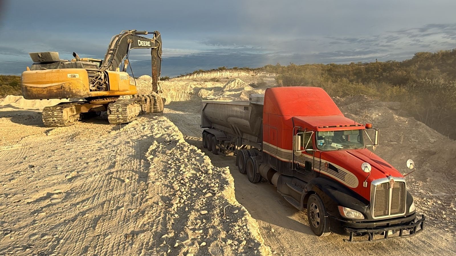 Excavadora cargando material en camión de volteo al atardecer